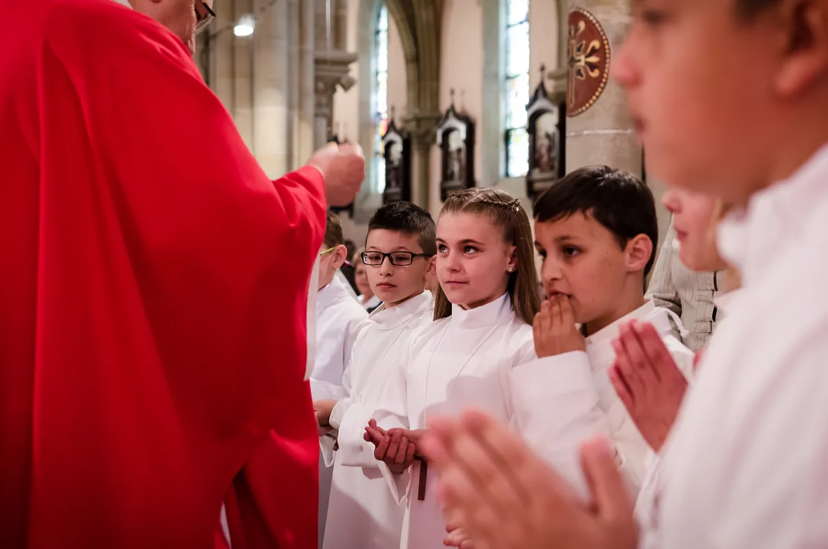 Reportage messe : communiants recevant la première hostie devant le prêtre lors d’une communion à Saint-Avold